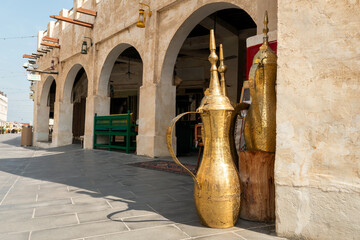 Traditional Arabic souvenirs and large golden coffee pots on display at Souq Waqif market in Doha, Qatar. Cultural Middle Eastern setting with vibrant details, no people.
