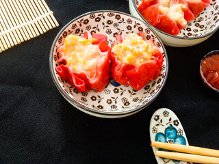 Red dimsum or Shumai or Siomay chicken and shrimp variance are served on decoration bowl,sauce,chopsticks, in black background.
