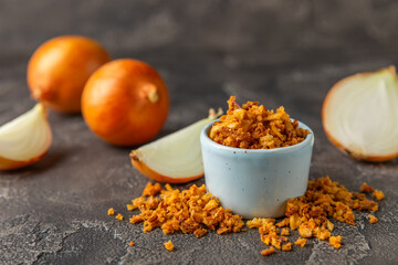 Crispy fried onions in a bowl on a wooden table. Roasted Onions. Seasoning for dishes. Spices. Salad dressing. Space for text. Copy space