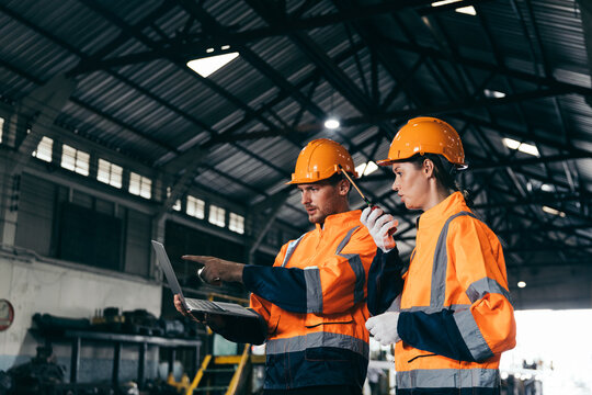 Two engineers wearing safety helmets and orange reflective jackets discuss industrial operate checking train maintenance at station, representing teamwork, safety and transportation and teamwork. - Powered by Adobe