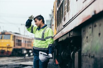 Tired railway engineer holding helmet while resting beside an old locomotive, reflecting exhaustion, hard work, dedication, and challenges in the railway maintenance industry.