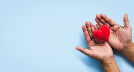 Hands gently holding a red heart symbol on light blue background, representing love, compassion, care, health support, giving, charity, kindness, hope, wellness, community, and emotional connection
