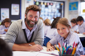 smiling male primary school teacher helping a student with writing at a clean desk, colorful but uncluttered classroom background