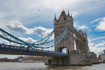 Obraz premium London's Tower Bridge over the Thames River: The iconic historic bridge stands against a partly cloudy sky, with reflections on the water's surface.