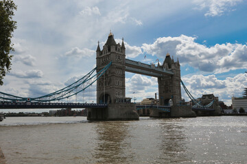 Obraz premium London's Tower Bridge over the Thames River: The iconic historic bridge stands against a partly cloudy sky, with reflections on the water's surface.