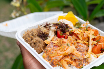 Vibrant Hawaiian poke plate with spicy ahi, salmon, and kalua pig held outdoors by a Black man’s...