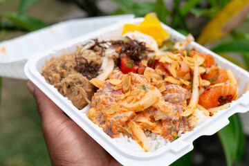 Vibrant Hawaiian poke plate with spicy ahi, salmon, and kalua pig held outdoors by a black man’s...
