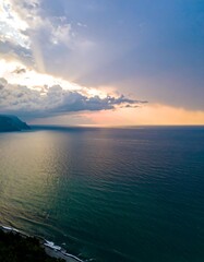 Fototapeta premium Panoramic view of a coastline at sunset. Calm ocean meets a dramatic cloudy sky