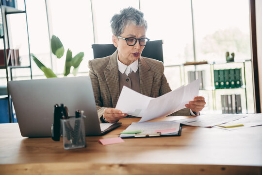 Senior businesswoman analyzing documents at her office desk in formal attire with confidence and professionalism