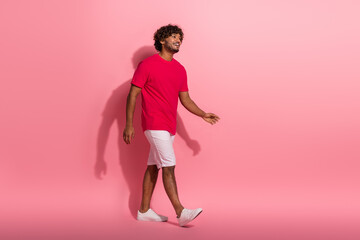 Cheerful young man in casual red t-shirt walking with a smile against a monochromatic pink backdrop