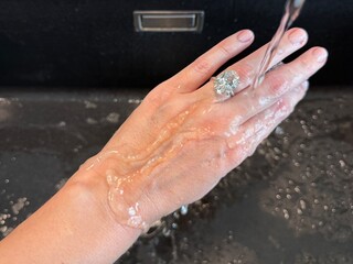 A landscape photo of a hand wearing a wedding band with oval diamond as water streams over the skin...