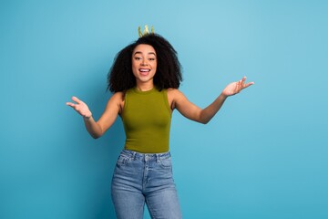 Cheerful young woman with curly hair in casual wear posing confidently against a bright blue...