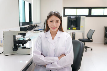 Scientist in laboratory wearing lab coat while standing next to microscope and smiling