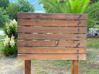 Closeup of wooden sign with multiple arrows set against palm background. Guidance, travel and orientation emphasizing navigation, tourism, and outdoor presence in natural landscape.