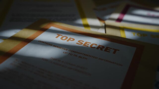 Camera pulls out from close up of Top Secret labeled manila folder in dark room. Classified and confidential government agency sensitive information. Conspiracy or leaked reports and files laid out