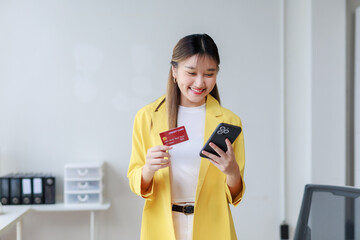 Young businesswoman using smartphone and credit card for online shopping in office