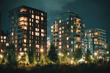 Obraz premium Urban apartment buildings illuminated at night with glowing windows and greenery in the foreground