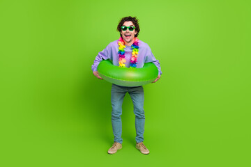 Young man enjoying leisure time with a green inflatable ring on a vibrant green background, wearing...