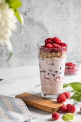 Granola with yogurt and fresh raspberries in glass on light background