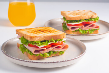 Close-up of two sandwiches with bacon, salami, prosciutto and fresh vegetables on rustic wooden cutting board. Club sandwich concept