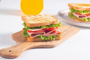 Close-up of two sandwiches with bacon, salami, prosciutto and fresh vegetables on rustic wooden cutting board. Club sandwich concept