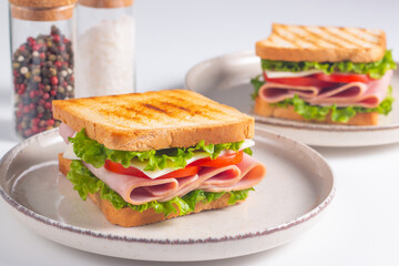 Close-up of two sandwiches with bacon, salami, prosciutto and fresh vegetables on rustic wooden cutting board. Club sandwich concept