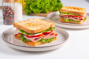 Close-up of two sandwiches with bacon, salami, prosciutto and fresh vegetables on rustic wooden cutting board. Club sandwich concept