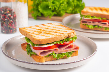Close-up of two sandwiches with bacon, salami, prosciutto and fresh vegetables on rustic wooden cutting board. Club sandwich concept