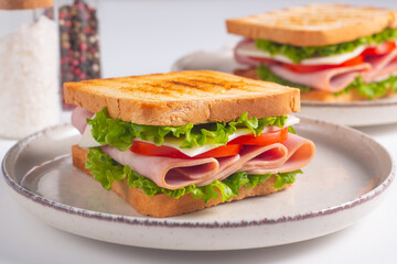 Close-up of two sandwiches with bacon, salami, prosciutto and fresh vegetables on rustic wooden cutting board. Club sandwich concept
