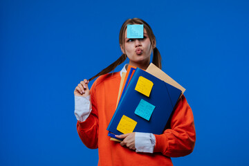 A young female student poses with a sticker on her forehead, holding folders and notes in her hands