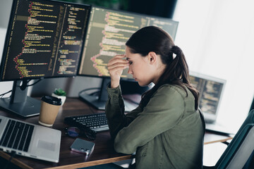Young female programmer stressed over coding issue at home workspace with multiple monitors showing...