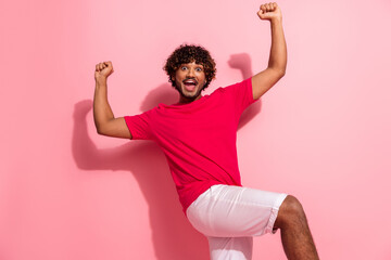 Energetic young man in a red t-shirt posing enthusiastically against a pink backdrop exuding...