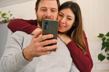 Loving mature couple using mobile phone. Husband and wife hugging, holding hands and looking at the...