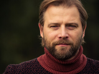 Portrait of handsome young man in wool knitted sweater outdoors. Male with long hair and beard feel...