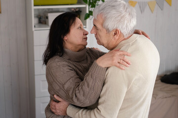 Fototapeta premium Senior couple hugging each other, kissing at home bedroom. Intimate Moment. Tender embrace between elderly age man and woman, husband and wife. Old people deep love. Time and feelings. Loving family