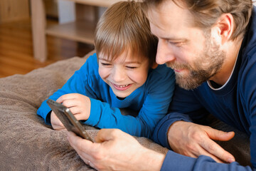Father and son little boy laughing and using phone. They watching funny videos together, playing...