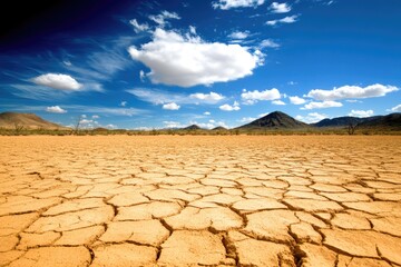 Dry, cracked earth under a vibrant blue sky with puffy white clouds and distant mountains