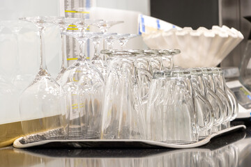Glass cups and wine glasses arranged upside-down on a drying rack on a metal surface of table in...