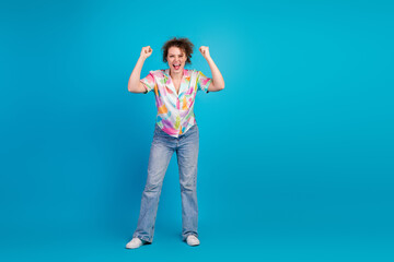 Excited young woman celebrating with joyful gestures on a vibrant blue background, wearing colorful...