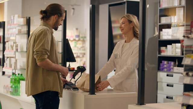 Pharmacist woman sell medicine in pharmacy cashier counter help customers buying medication health care service medical prescription drugstore order using contactless payment buy pills drugs vitamins