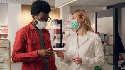 African man customer in pharmacy health care Caucasian woman pharmacist in mask coronavirus antiviral pills drugs medicine health protection covid illness viral infection remedy doctor help patient
