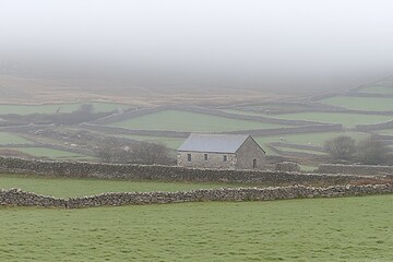 Misty valley with stone walls and a small stone building