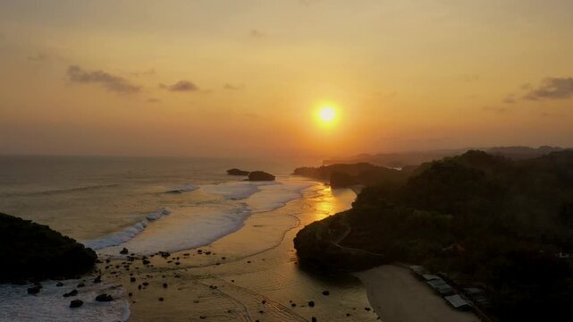A stunning sunset over Watu Karung Beach in Pacitan, Indonesia, captures the golden hour light reflecting on the wet sand. Aerial Beach Sunset indonesia