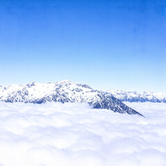 Snowy Mountain Peaks Above Clouds Against a Clear Blue Sky