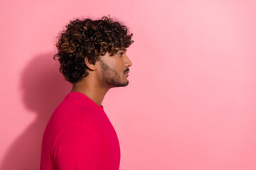 Side profile portrait of a stylish young man with curly hair wearing a red t-shirt against a pink...