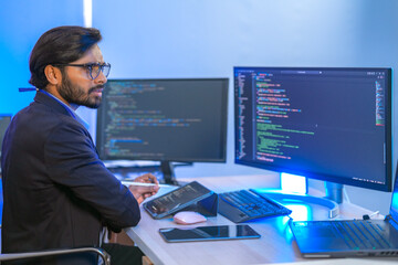 A focused software developer codes on his laptop while analyzing complex data on a large monitor. A...