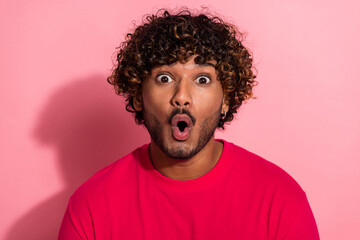 Portrait of a young man expressing surprise with wide eyes and open mouth wearing casual red shirt on pink background