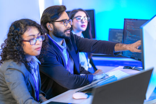 A senior software developer or team lead points at code on a screen, mentoring a female colleague. Diverse professionals collaborating on a project in a modern IT office. - Powered by Adobe