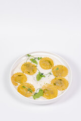 Top view of a plate with ravioli pasta with cheese and sauce on a white background