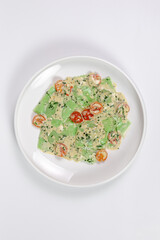 Green vegan ravioli with creamy sauce and cherry tomatoes, top view